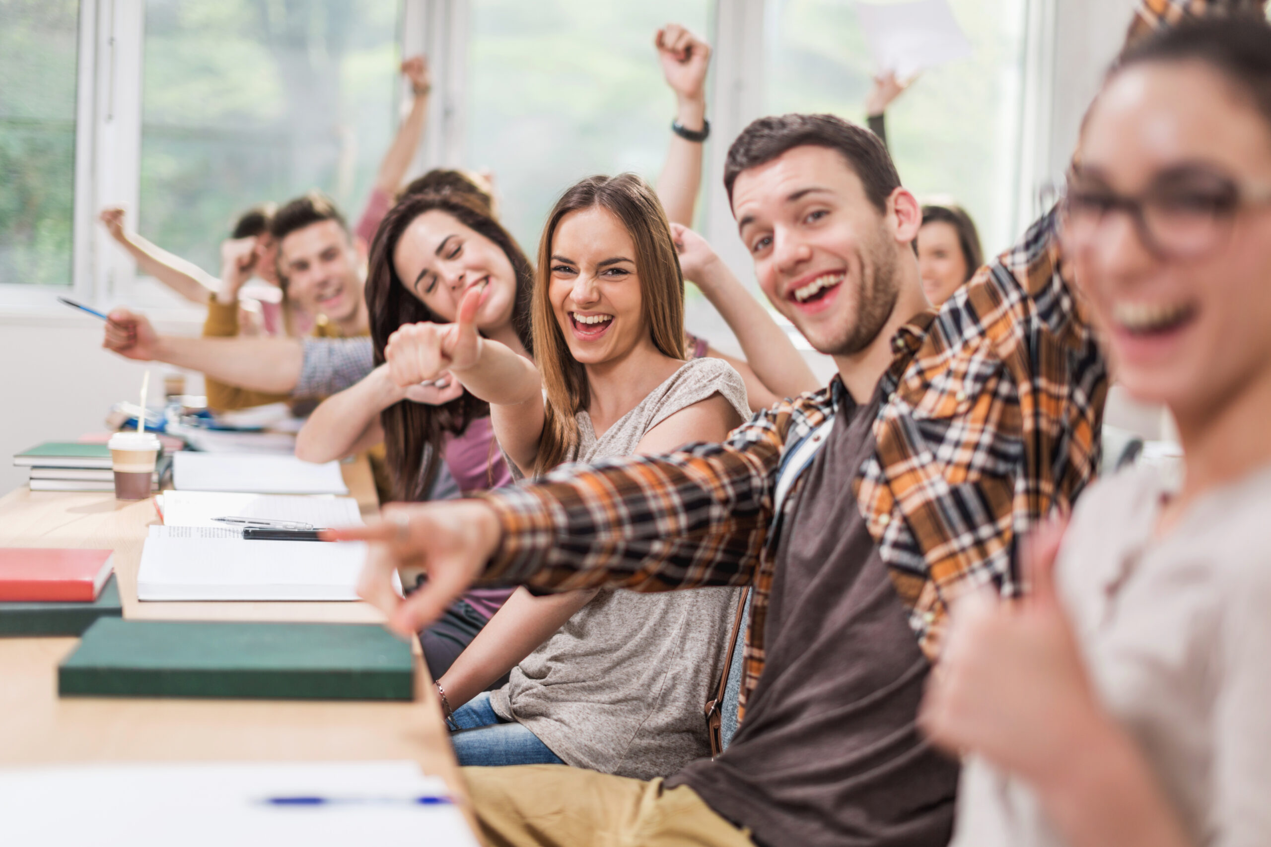 Cheerful students celebrating in classroom and looking at camera